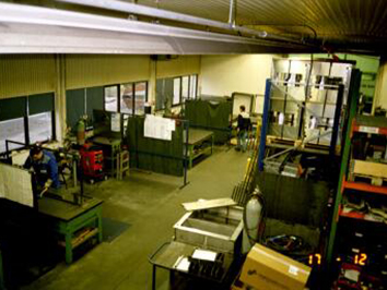Eine industrielle Werkshalle mit mehreren Arbeitsstationen, Werkbänken und Mitarbeitern, die an Metallverarbeitung arbeiten.