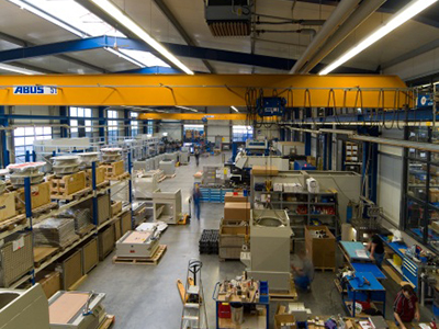 Innenansicht einer modernen Produktionshalle mit einer großen ABUS-Krananlage und zahlreichen Werkstationen.